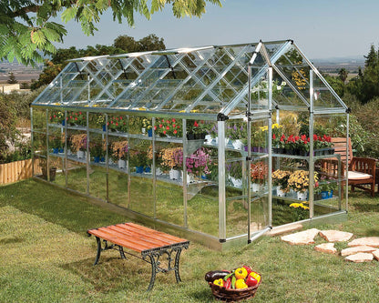 Large glass greenhouse with plants on a grassy area with a wooden bench and fruit basket.